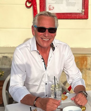 Mature male lifestyle model wearing sunglasses seated at outdoor cafe