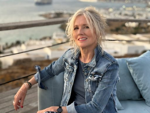 Mature lifestyle model seated outdoors wearing denim jacket by waterfront