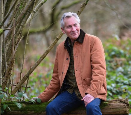 Mature lifestyle model seated outdoors in woodland setting wearing jacket